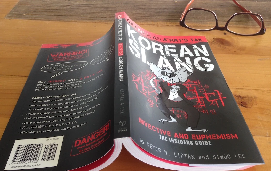 Korean Slang photographed on a wooden table, showing the paperback’s front, spine and back cover